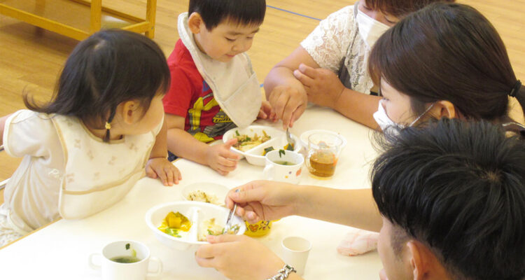 保育園で先生と保護者と食事をする園児の様子