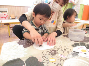 保育園で工作をする園児の手伝う先生の様子